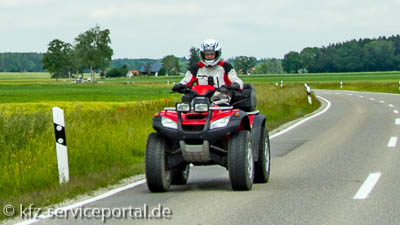 Ein fahrendes Quad auf einer Landstraße. Der Fahrer trägt Sicherheitskleidung.