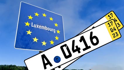Vor einem Grenzschild von Luxemburg sind Kurzzeitkennzeichen zu sehen und symbolisiert, dass Fahrten in das Ausland damit nicht immer zulässig sind.