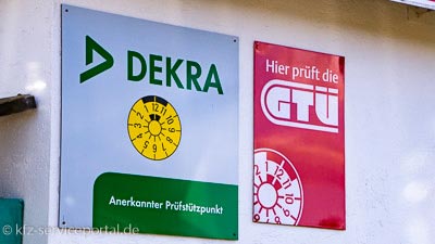 An einer Hauswand sind zwei Schilder angebracht. Diese besagen, dass in diesem Betrieb DEKRA und GTÜ prüft.