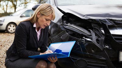 Eine Sachverständige untersucht ein Fahrzeug und macht sich Notizen
