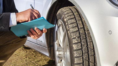 Ein Sachverständiger ist vor einem Fahrzeug zu sehen. Er macht sich Notizen zum Fahrzeugzustand.