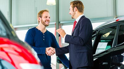 Ein Kunde und ein Fahrzeughändler schütteln sich die Hände. Beide sind sehr zufrieden.