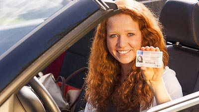 Eine junge Frau zeigt mit freudigem Gesichtsausdruck den Führerschein vor.