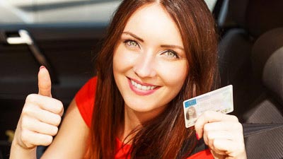 Eine junge Frau zeigt mit freundlichem Gesicht ihren Führerschein.