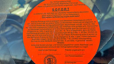 Auf der Seitenscheibe eines Autos klebt ein orangefarbener Aufkleber. Das muss sofort von diesem Stellplatz entfernt werden, da es keine Zulassung hat.