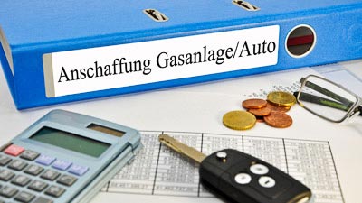 Ein Ordner mit der Aufschrift Anschaffung Gasanlage/Auto mit Unterlagen, Taschenrechner und Autoschlüssel.