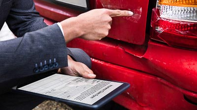 Das Heck eines Autos ist beschädigt. Ein Prüfer kontrolliert den Schaden und macht sich Notizen.