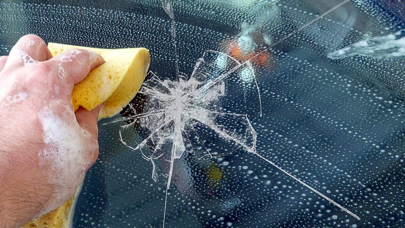 Das Heck eines Autos ist beschädigt. Ein Prüfer kontrolliert den Schaden und macht sich Notizen.