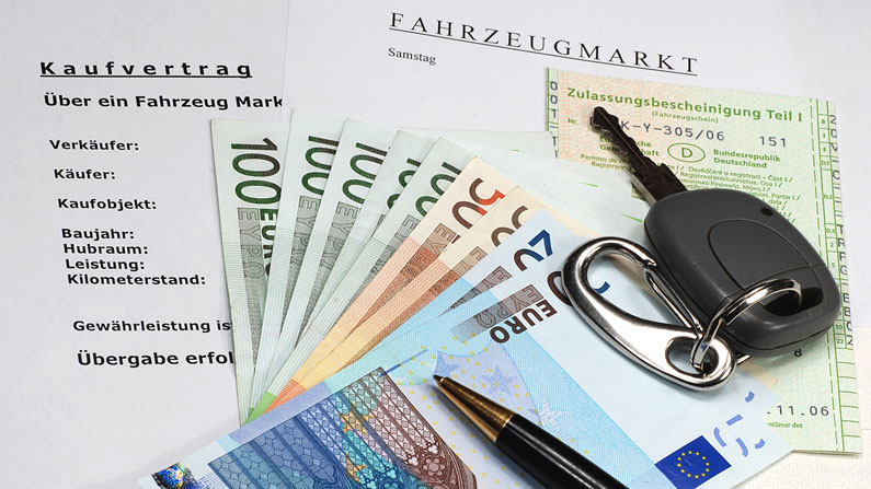 Kaufvertrag für ein Auto, eine Zulassungsbescheinigung, Geldscheine, ein Autoschlüssel und ein Kugelschreiber liegen auf einem Tisch