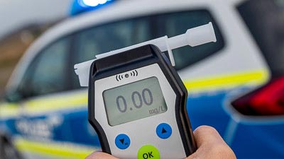 Im Vordergrund sieht man ein Gerät zur Alkoholkontrolle. Im Hintergrund steht ein Polizeifahrzeug.
