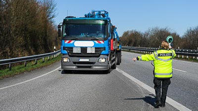 Eine Polizistin winkt mit einer Polizeikelle einen Lastkraftwagen auf einen Parkplatz zu einer Kontrolle.