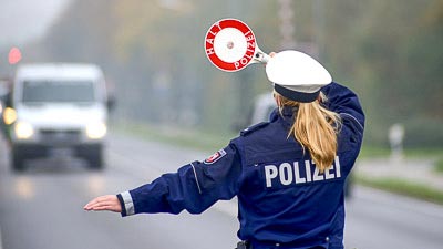 Im Vordergrund steht eine Polizistin mit einer Kelle und winkt einen LKW zur Kontrolle auf einen Parkplatz.