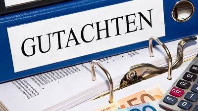 Ein Ordner mit der Aufschrift Gutachten liegt auf einem geöffneten Ordner mit Unterlagen.