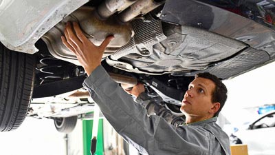 Ein Sachverständiger prüft ein Auto auf einer Hebebühne. Er kontrolliert die Abgasanlage.