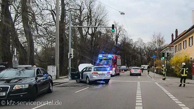 Bei einem Unfall sperrt die Feuerwehr die Straße. Der Einsatzwagen hat das Blaulicht angeschaltet. Das Unfallfahrzeug steht mit offener Motorhaube mitten auf der Straße.