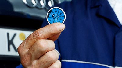 Ein Prüfer hält eine HU-Prüfplakette in seinen Fingern.