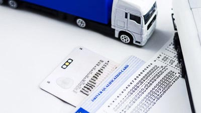 Zu sehen ist eine Fahrerkarte, ein Spielzeuglastwagen und ein Kontrollausdruck der Fahr- und Ruhezeiten.