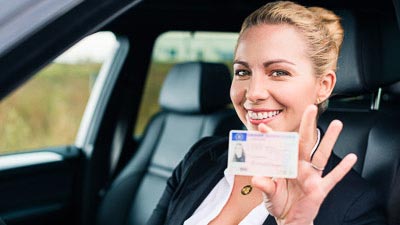 Eine junge Frau sitzt in einem Auto und hält einen Führerschein zwischen den Fingern.