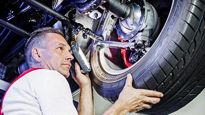 Der Prüfer einer Kfz-Prüfstelle kontrolliert ein Fahrzeug von unten.