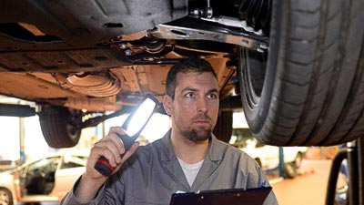 Ein Sachverständiger prüft ein Auto auf einer Hebebühne. Er kontrolliert die Aufhängung und Räder.