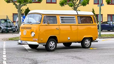 Ein orangefarbener VW Bulli Oldtimer fährt auf der Straße.