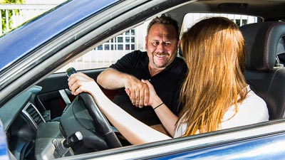 Ein Fahrlehrer gratuliert einer Fahrschülerin im Auto zur bestandenen Fahrprüfung.