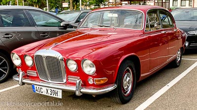 Auf einem Parkplatz steht ein roter Jaguar-Oldtimer mit einem H-Kennzeichen.