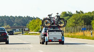 Ein PKW zieht einen Anhänger, auf welchem Fahrräder quer transportiert werden.