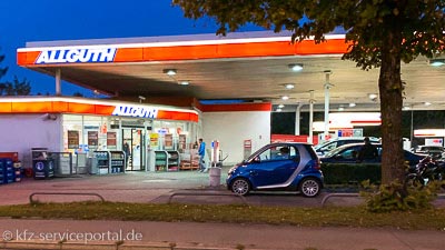 Eine Tankstelle in Dämmerung. Die Reklame und Zapfsäulen sind beleuchtet.