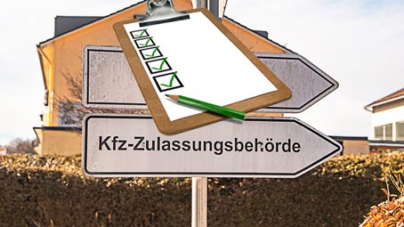 Ein Straßenschild zeigt den Weg zur Zulassungsbehörde. Darauf ist ein Klemmbrett mit einer Unterlagen Checkliste zu sehen.