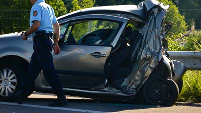 Ein Totalschaden eines PKWs im Ausland. Ein Polizist des Landes nimmt den Unfall auf.