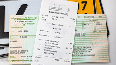 Eine Einzahlungsquittung für die Zulassung der Kurzzeitkennzeichen liegt auf dem Fahrzeugschein und den Schildern mit dem gelben Rand.