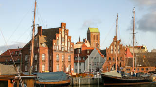 Der historische alte Hafen in Wismar gehört zum UNESCO Kulturerbe, am Hafenufer liegen Segelschiffe und der Blick richtet sich in die Altstadt